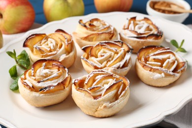 Photo of Tasty apple roses with powdered sugar served on table, closeup