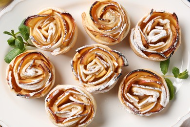 Photo of Tasty apple roses with powdered sugar on plate, top view