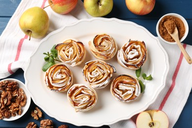 Photo of Tasty apple roses with powdered sugar served on blue wooden table, flat lay