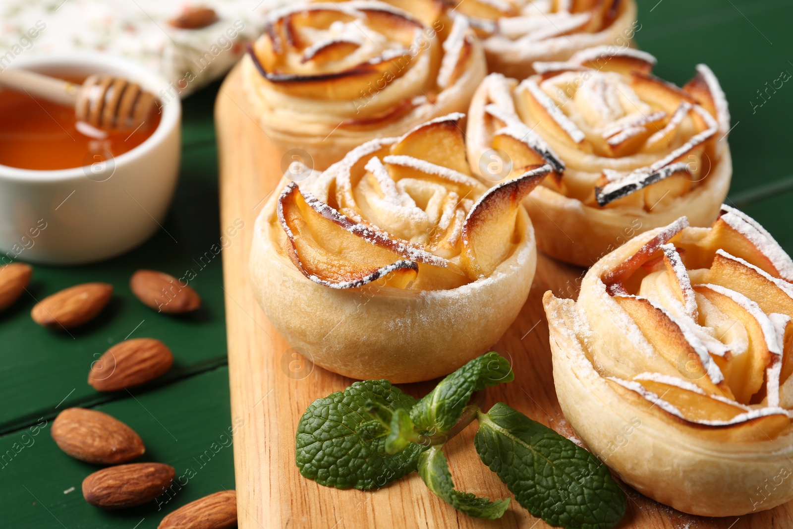 Photo of Tasty apple roses with powdered sugar served on green wooden table, closeup