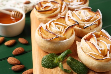 Photo of Tasty apple roses with powdered sugar served on green wooden table, closeup