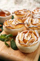 Photo of Tasty apple roses with powdered sugar served on green table, closeup