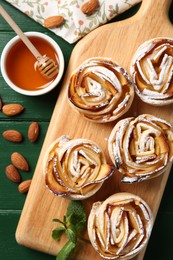 Photo of Tasty apple roses with powdered sugar served on green wooden table, flat lay