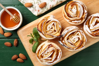 Photo of Tasty apple roses with powdered sugar served on green wooden table, flat lay