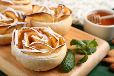Photo of Tasty apple roses with powdered sugar served on green wooden table, closeup