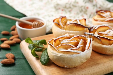 Photo of Tasty apple roses with powdered sugar served on green wooden table, closeup