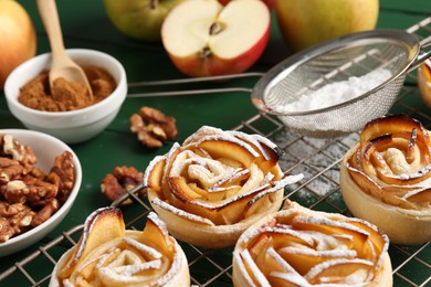 Photo of Tasty apple roses with powdered sugar served on green wooden table, closeup