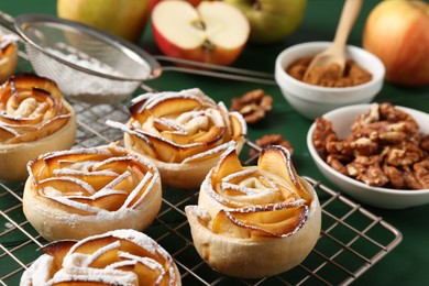 Photo of Tasty apple roses with powdered sugar served on green wooden table, closeup