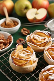 Photo of Tasty apple roses with powdered sugar served on green wooden table, closeup