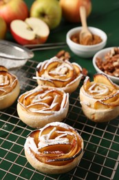 Photo of Tasty apple roses with powdered sugar served on green wooden table, closeup