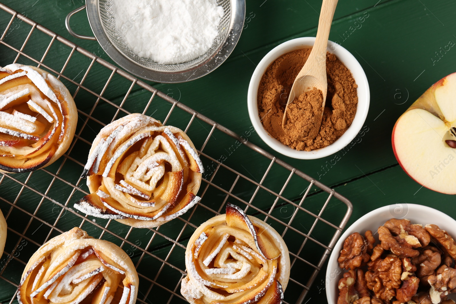 Photo of Tasty apple roses with powdered sugar served on green wooden table, flat lay