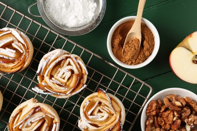 Photo of Tasty apple roses with powdered sugar served on green wooden table, flat lay