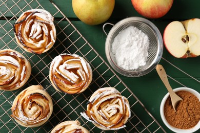 Photo of Tasty apple roses with powdered sugar served on green wooden table, flat lay