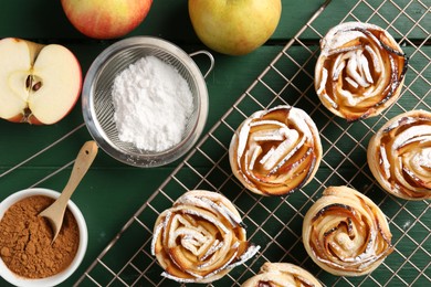 Photo of Tasty apple roses with powdered sugar served on green wooden table, flat lay