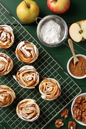 Photo of Tasty apple roses with powdered sugar served on green wooden table, flat lay