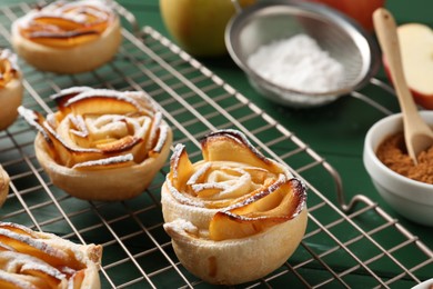 Photo of Tasty apple roses with powdered sugar served on green wooden table, closeup