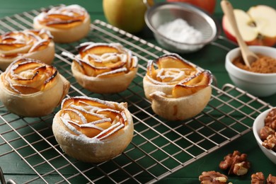 Photo of Tasty apple roses with powdered sugar served on green wooden table, closeup