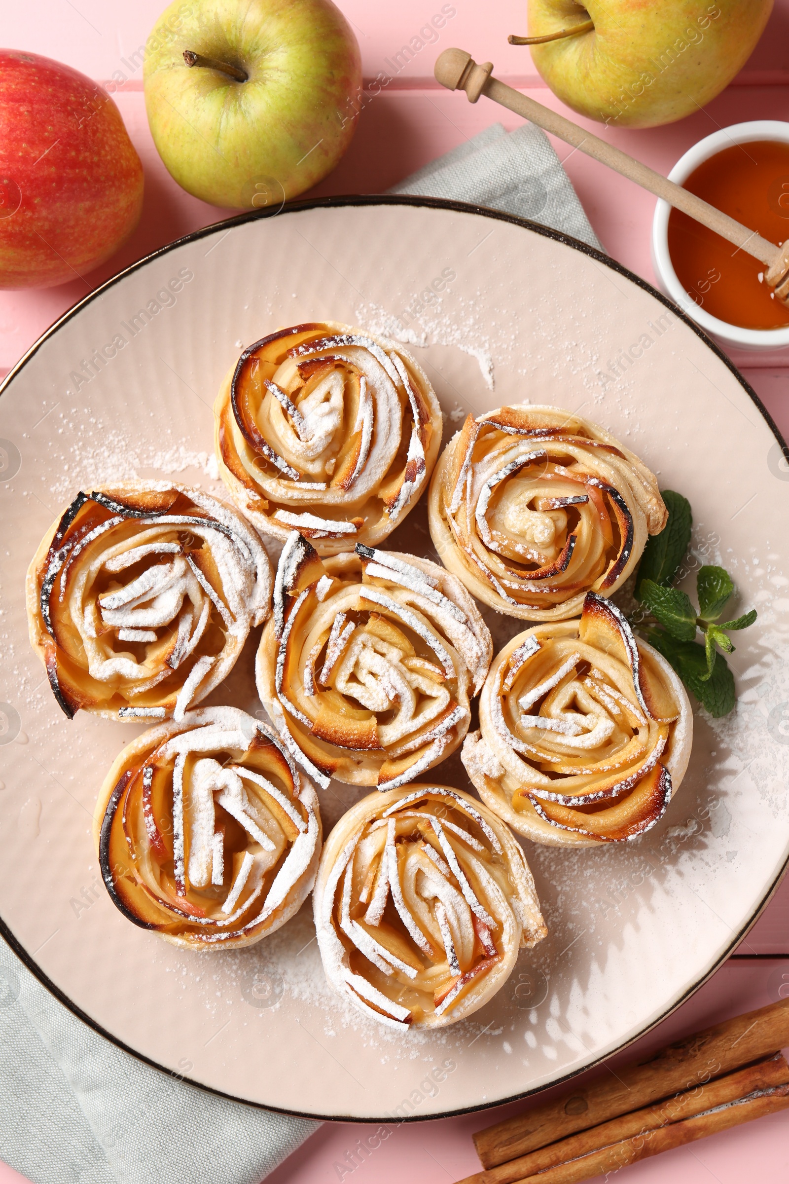 Photo of Tasty apple roses with powdered sugar served on pink wooden table, flat lay