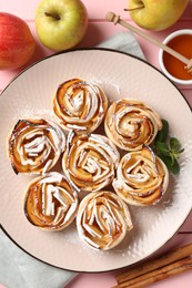 Photo of Tasty apple roses with powdered sugar served on pink wooden table, flat lay