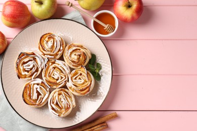Photo of Tasty apple roses with powdered sugar served on pink wooden table, flat lay. Space for text