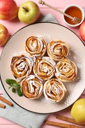 Photo of Tasty apple roses with powdered sugar served on pink wooden table, flat lay