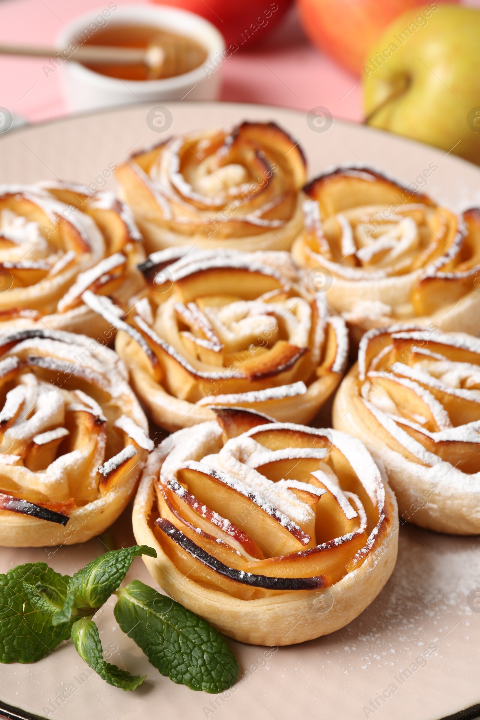 Photo of Tasty apple roses with powdered sugar served on table, closeup