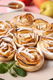 Photo of Tasty apple roses with powdered sugar served on table, closeup