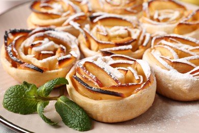 Photo of Tasty apple roses with powdered sugar served on table, closeup