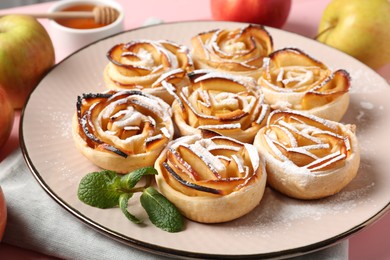 Photo of Tasty apple roses with powdered sugar served on pink table, closeup