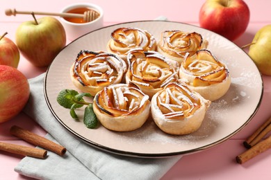 Photo of Tasty apple roses with powdered sugar served on pink wooden table, closeup