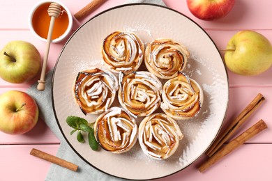Photo of Tasty apple roses with powdered sugar served on pink wooden table, flat lay