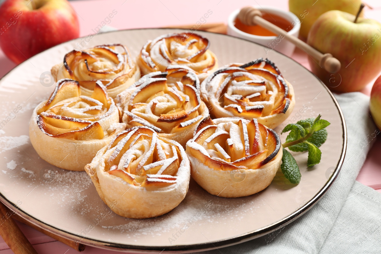 Photo of Tasty apple roses with powdered sugar served on pink wooden table, closeup
