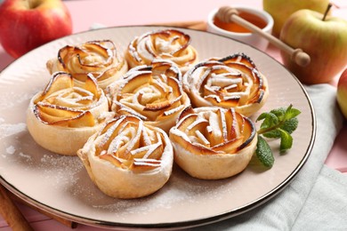 Photo of Tasty apple roses with powdered sugar served on pink wooden table, closeup
