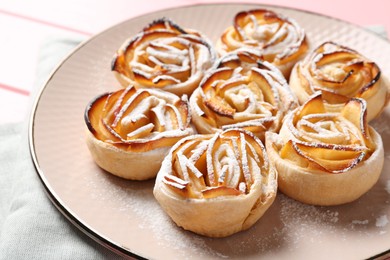 Photo of Tasty apple roses with powdered sugar on pink table, closeup