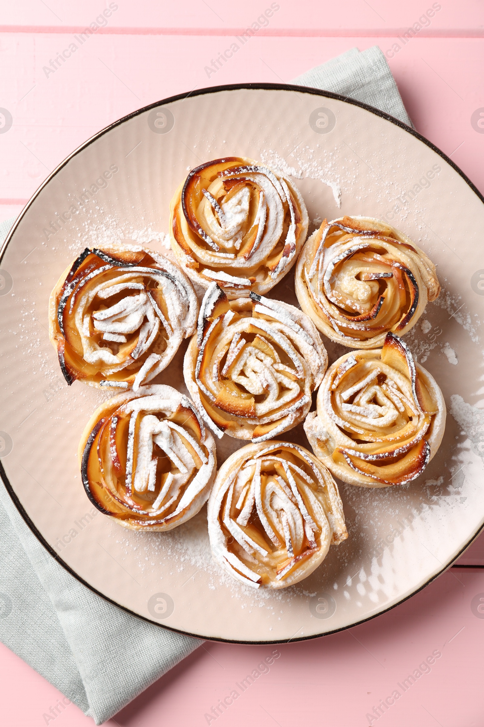 Photo of Tasty apple roses with powdered sugar on pink wooden table, top view