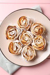 Photo of Tasty apple roses with powdered sugar on pink wooden table, top view