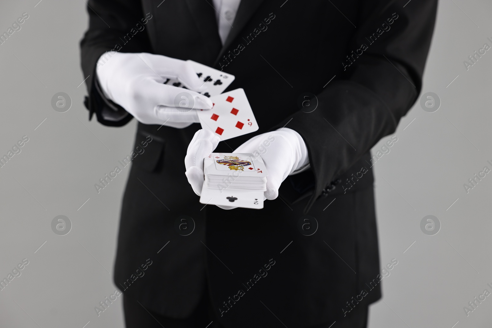 Photo of Illusionist showing trick with playing cards on grey background, closeup