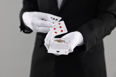 Photo of Illusionist showing trick with playing cards on grey background, closeup