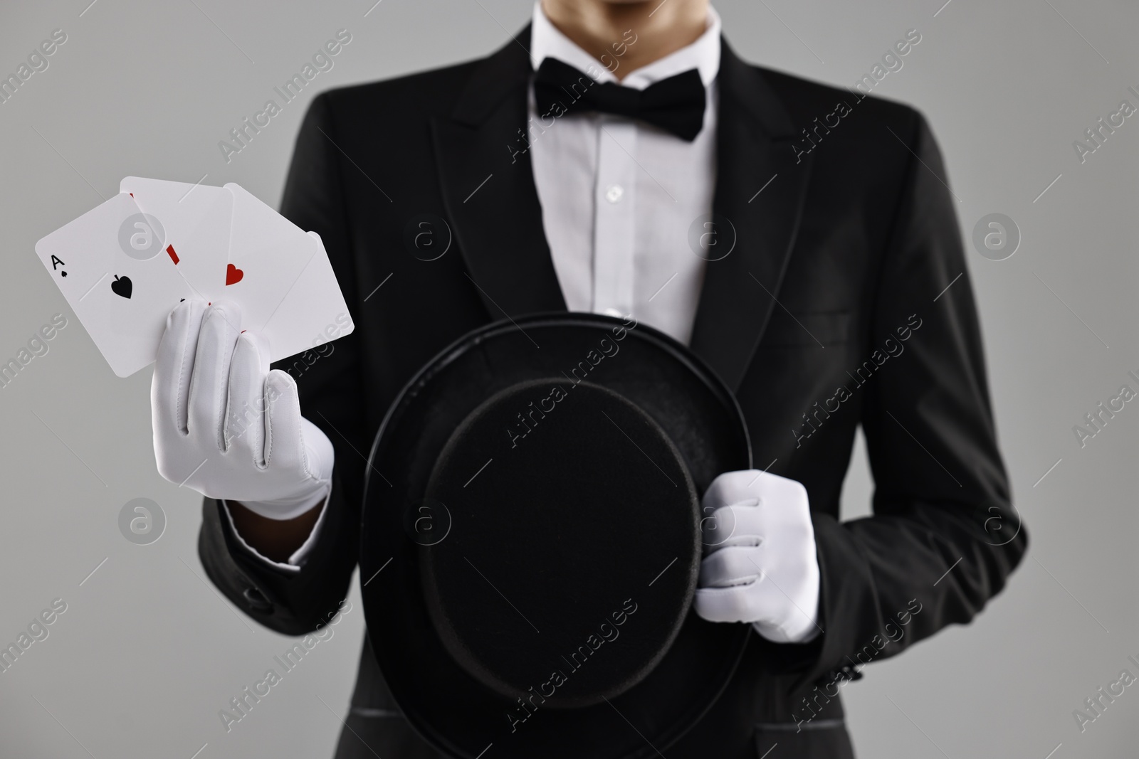 Photo of Illusionist with top hat showing playing cards on grey background, closeup