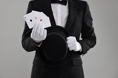 Photo of Illusionist with top hat showing playing cards on grey background, closeup