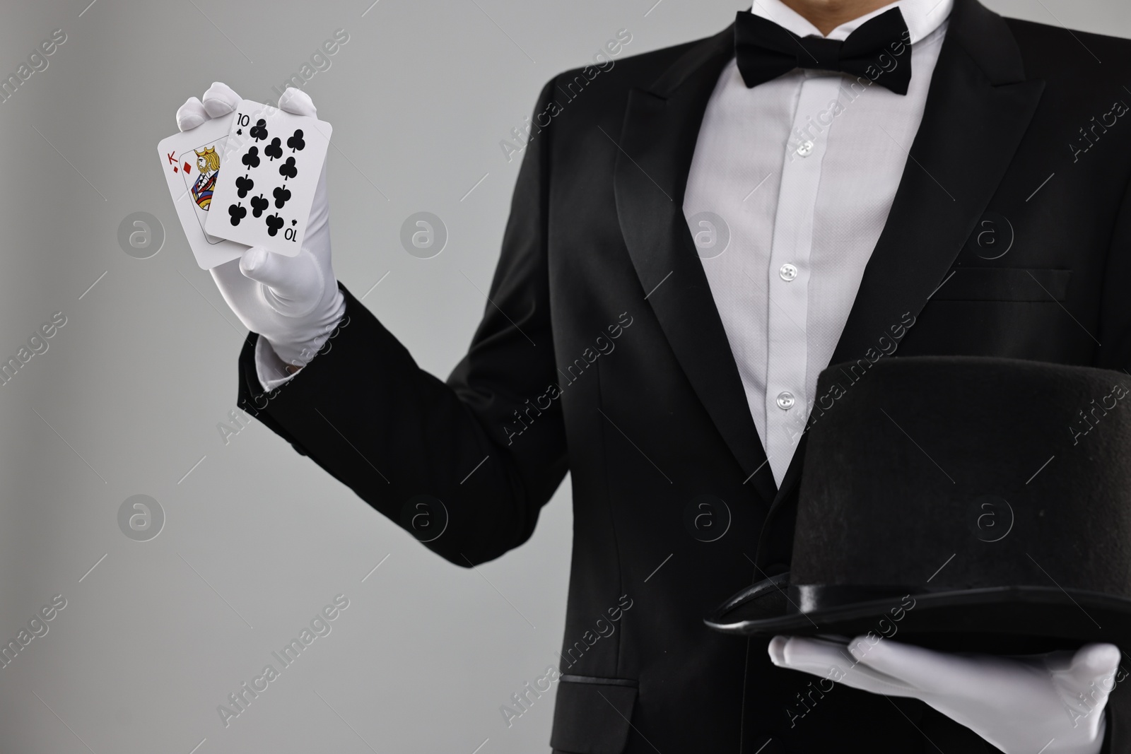 Photo of Illusionist with top hat showing playing cards on grey background, closeup