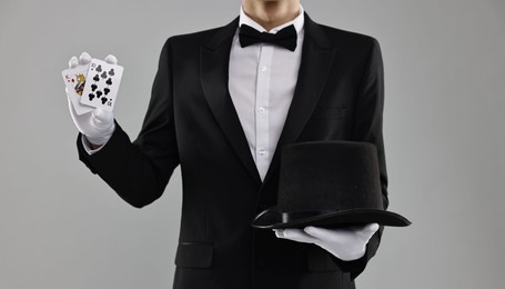 Photo of Illusionist with top hat showing playing cards on grey background, closeup