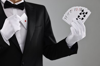 Photo of Illusionist hiding one playing card behind jacket lapel while showing deck on grey background, closeup