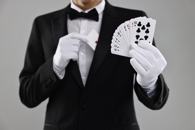 Photo of Illusionist hiding one playing card behind jacket lapel while showing deck on grey background