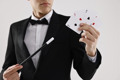 Photo of Illusionist pointing magic wand on playing cards against white background, closeup