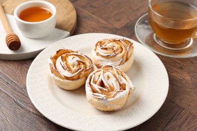 Photo of Freshly baked apple roses, honey and tea on wooden table, closeup