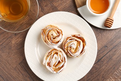 Photo of Freshly baked apple roses, honey and tea on wooden table, flat lay