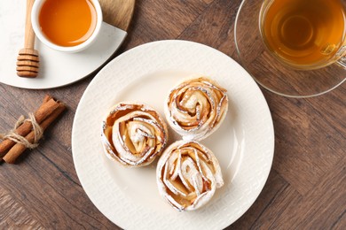 Photo of Freshly baked apple roses, honey, cinnamon sticks and tea on wooden table, flat lay