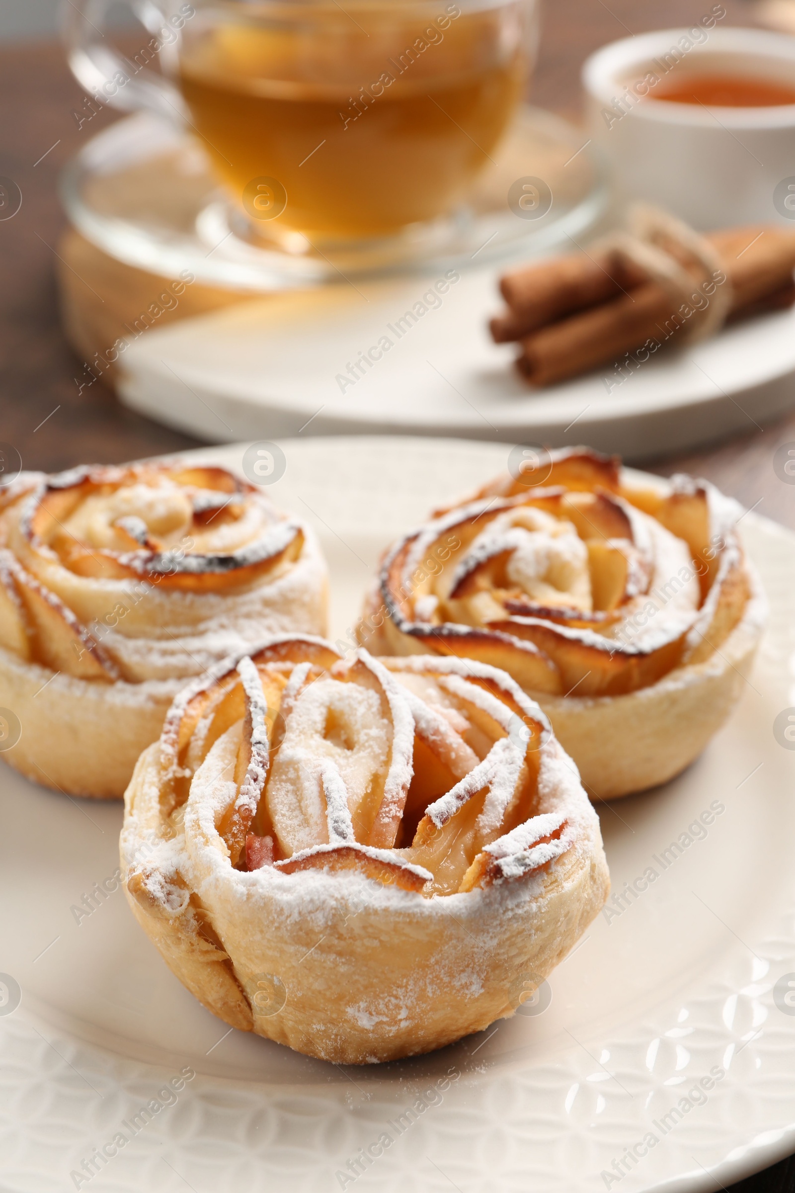Photo of Freshly baked apple roses, honey, cinnamon sticks and tea on table, closeup