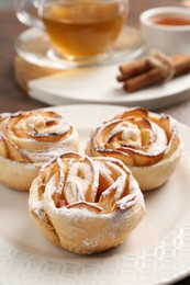 Photo of Freshly baked apple roses, honey, cinnamon sticks and tea on table, closeup